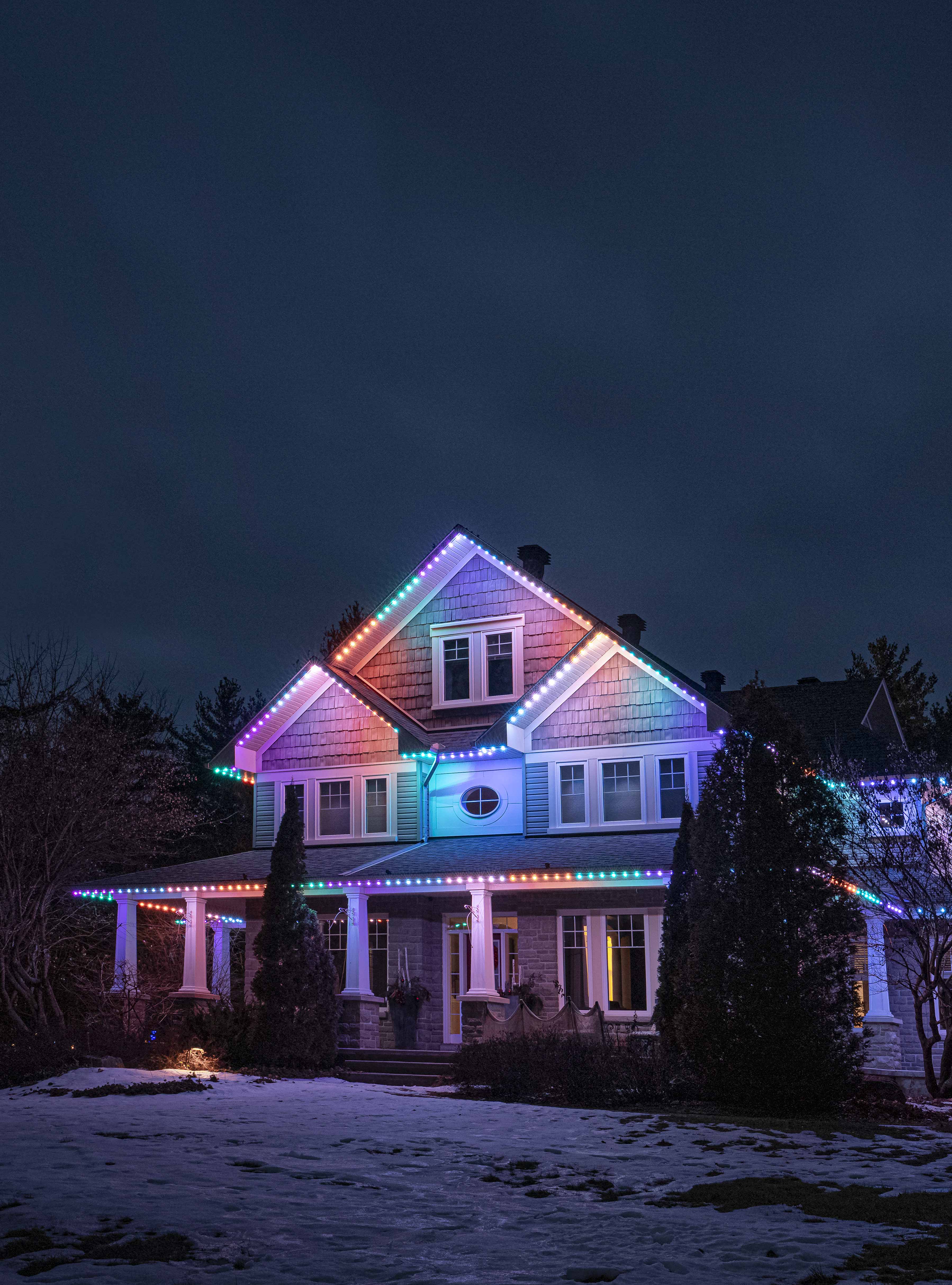 Two-story house with permanent holiday lighting in colorful patterns along the roofline.